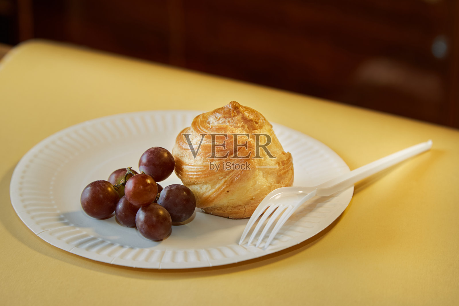 阳光下的白色盘子上的泡芙与葡萄,背景为黄色,甜点展示在白色盘子上照片摄影图片
