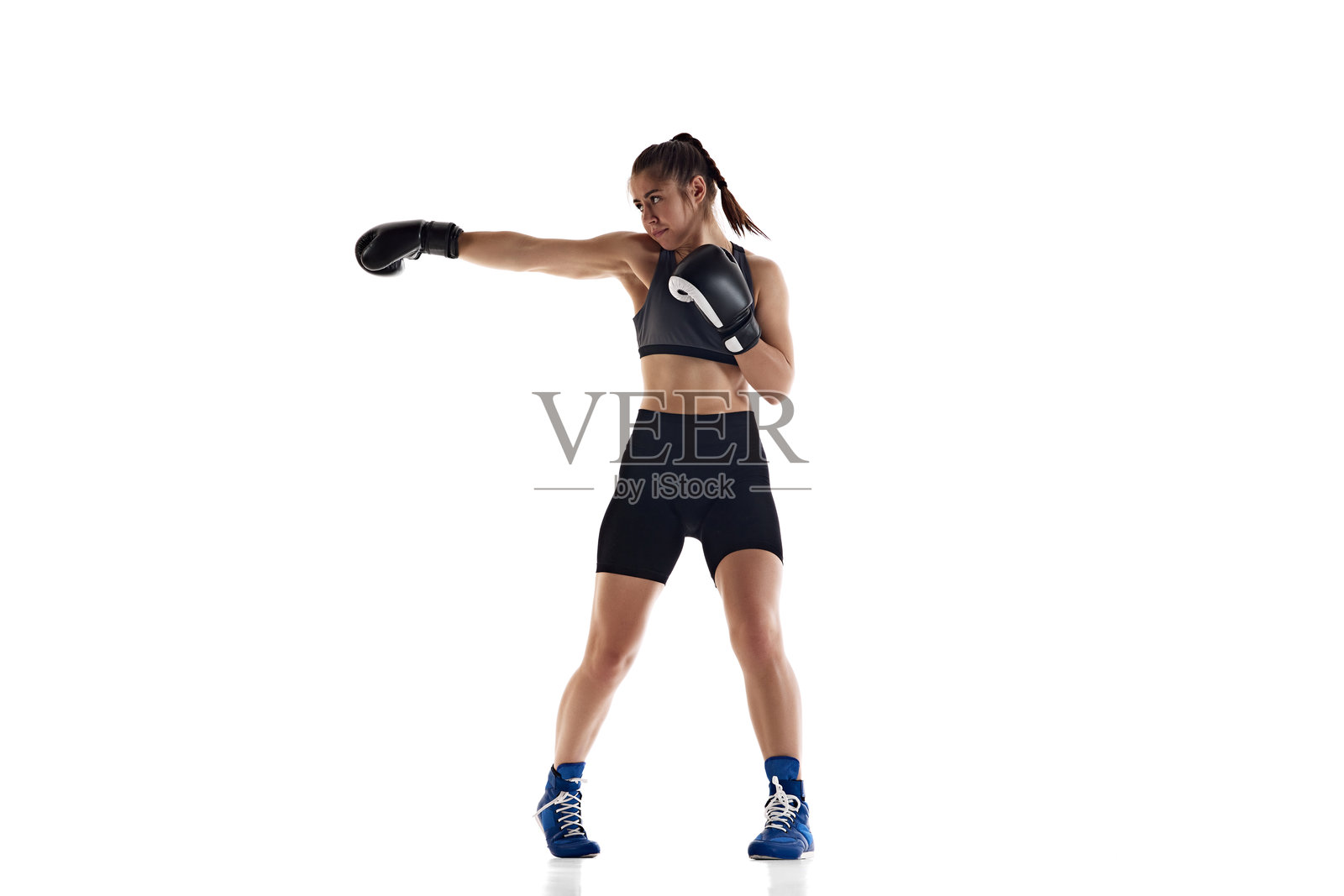 刺拳。一位表情严肃、注意力集中的年轻女子全身像,她拥有运动型身材,是一名拳击运动员,在白色工作室背景下进行训练照片摄影图片