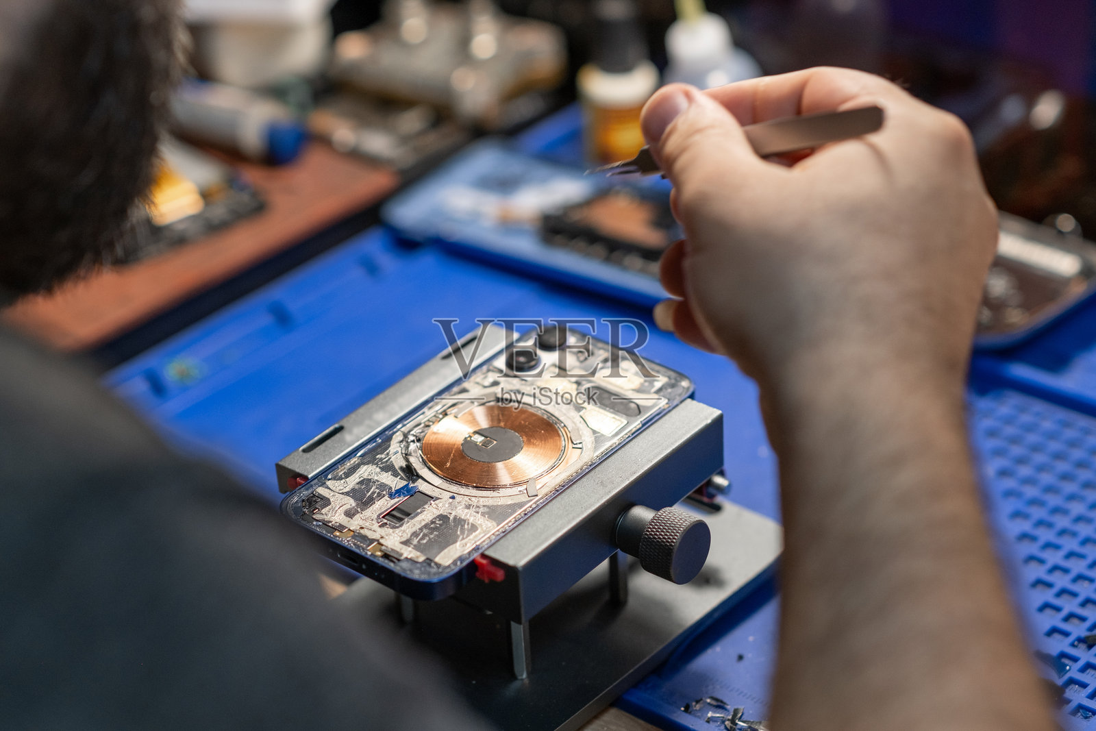 一名技术人员在一个干净整洁的工作室里仔细修理智能手机并更换电池,周围有各种工具。照片摄影图片