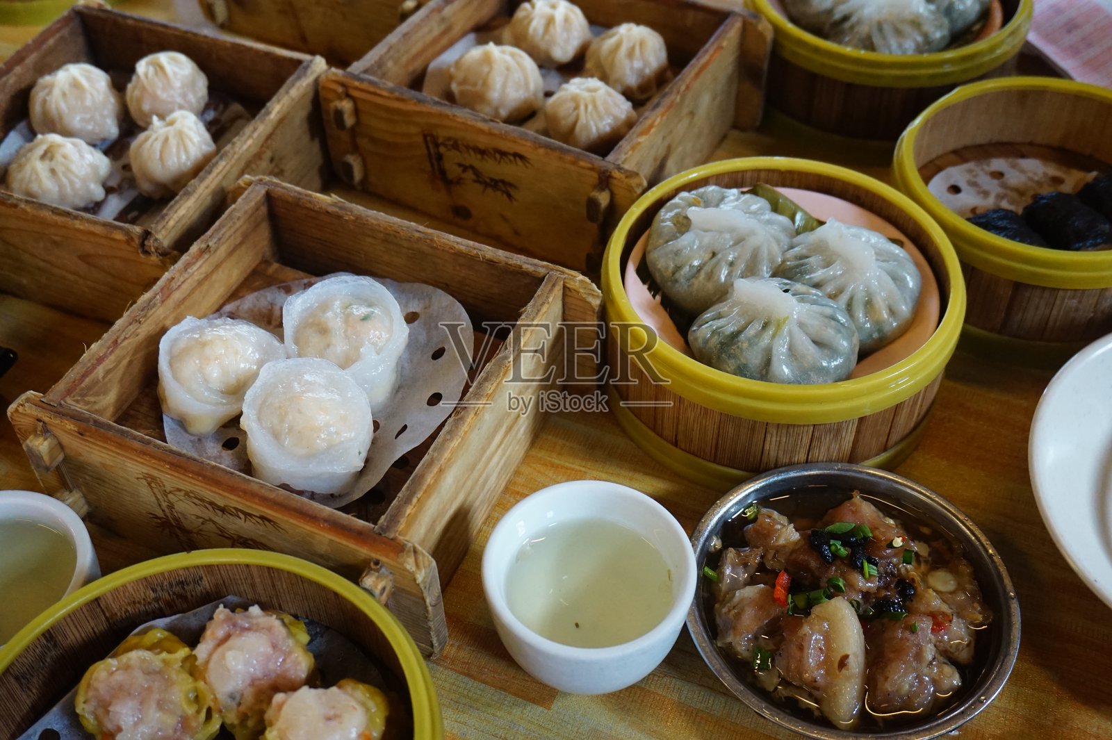 木桌上的金属碗里盛着传统的中式点心。桌上有许多不同种类的食物和饮料。照片摄影图片