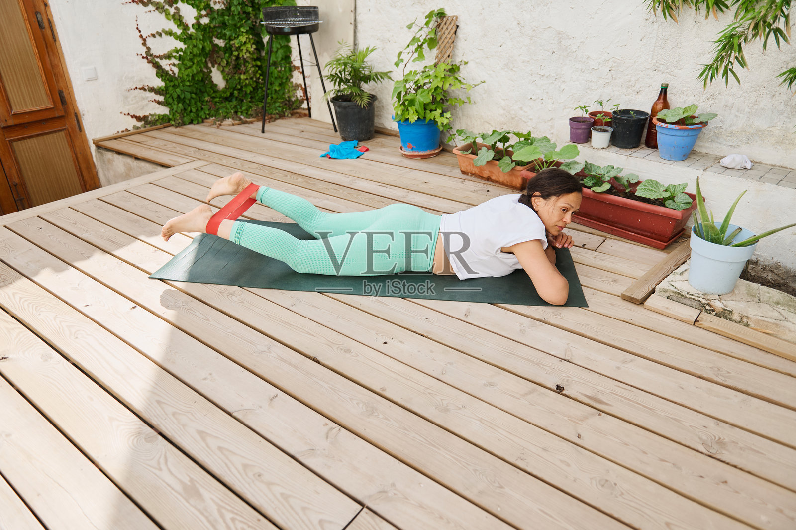 女人在木质甲板上练习户外瑜伽,身边有花盆植物和阻力带。照片摄影图片