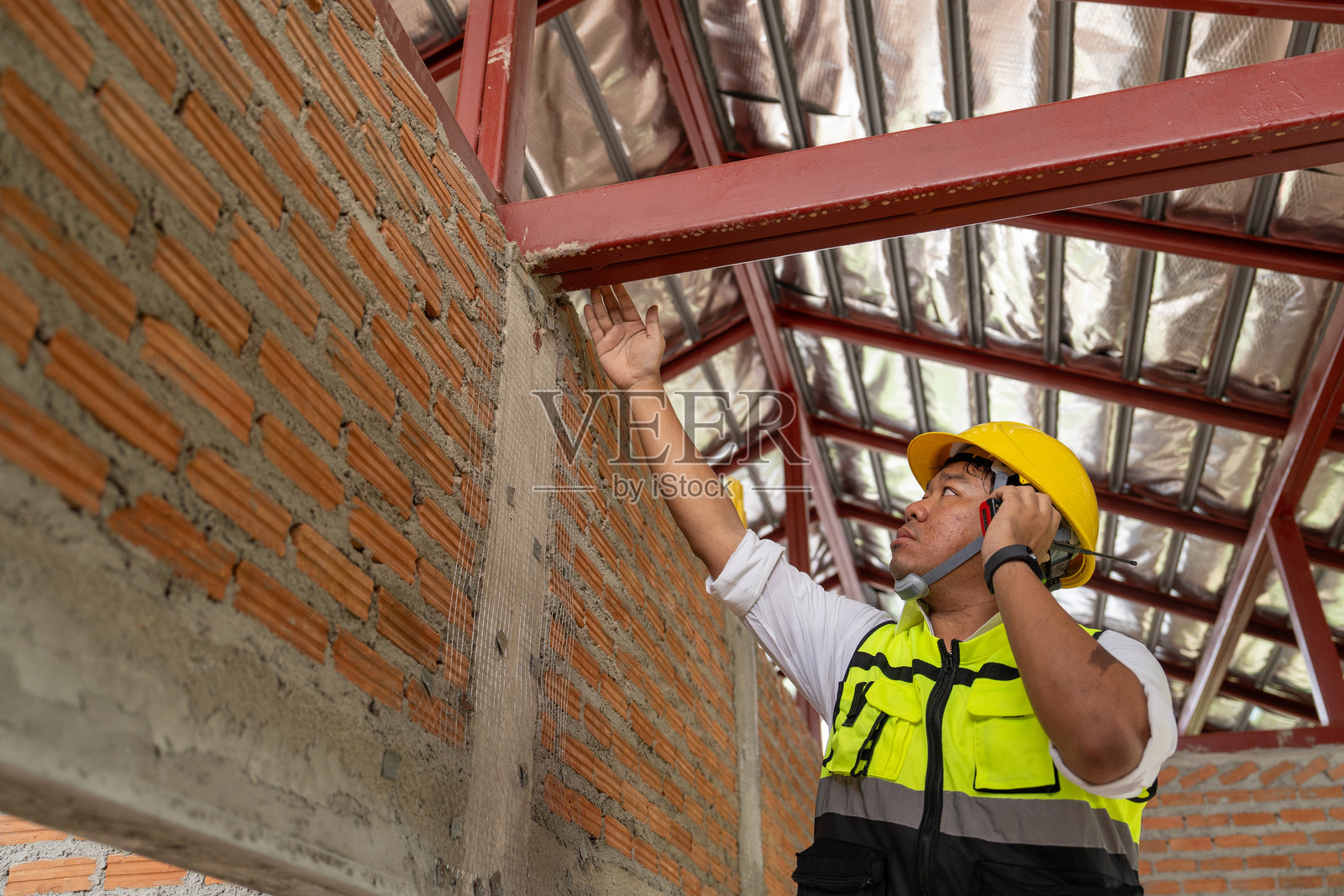 亚洲男性建筑工人在施工现场控制和检查钢屋顶结构的质量工作。照片摄影图片