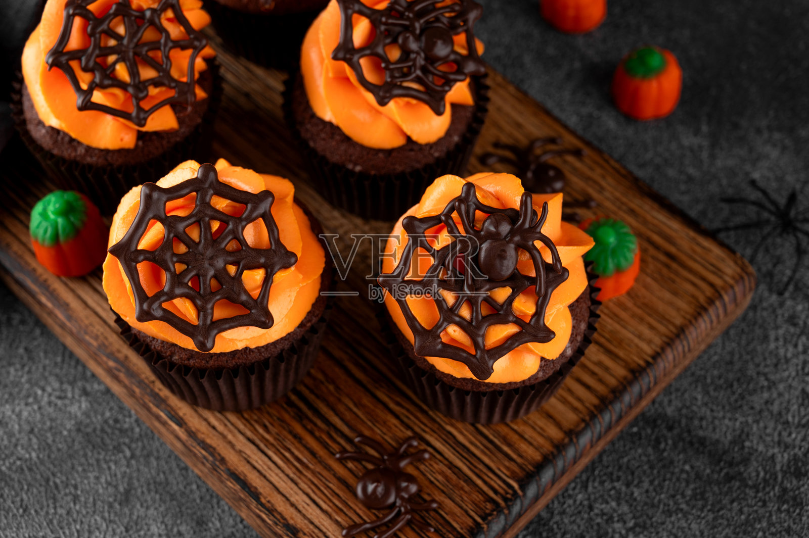 万圣节巧克力杯子蛋糕,配有橙色糖霜和巧克力蜘蛛网,背景为深色。节日甜点。搞笑食品创意。留白空间。照片摄影图片