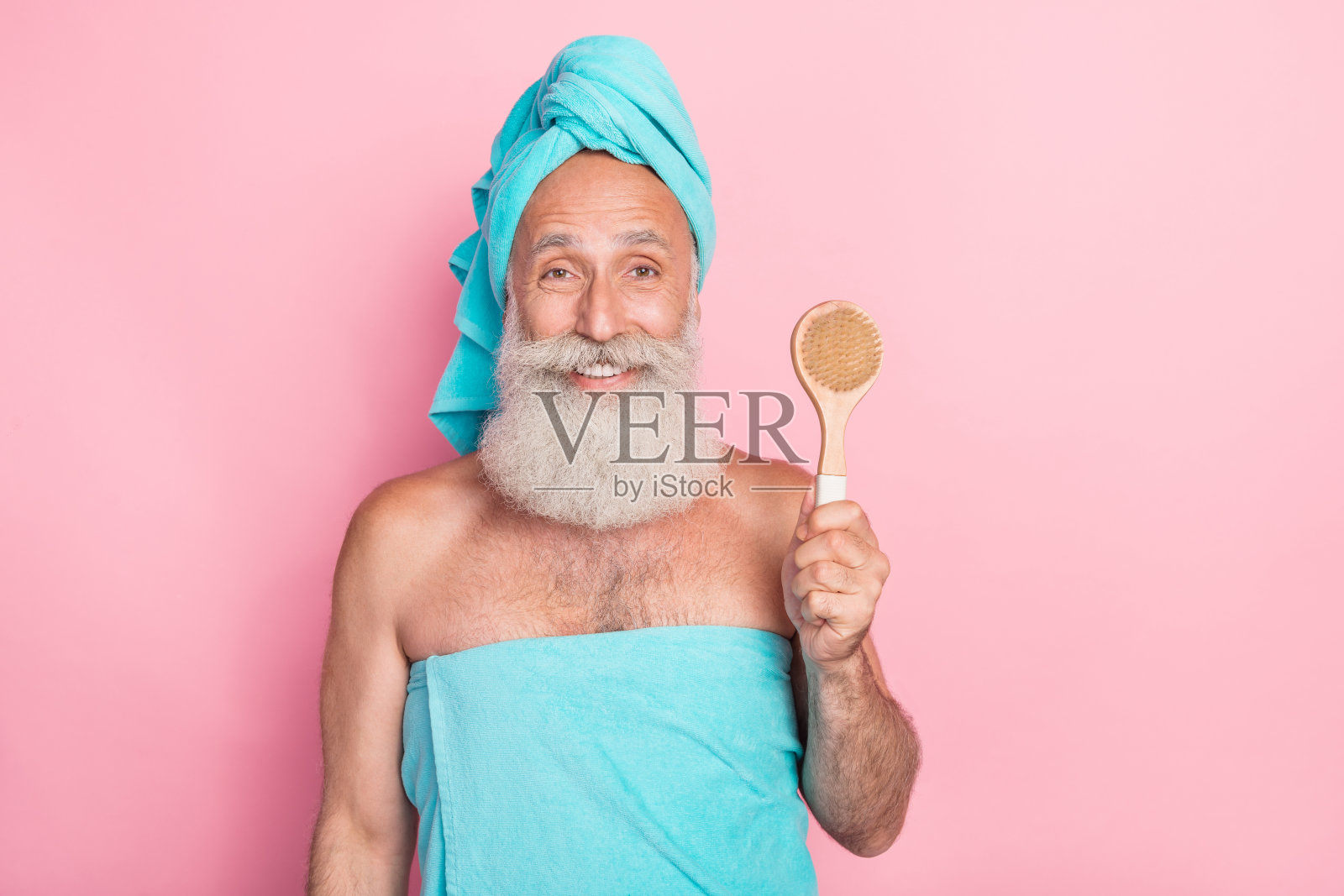 退休老年男子手持按摩器清洁柔软脱皮肌肤,背景为柔和色彩。照片摄影图片