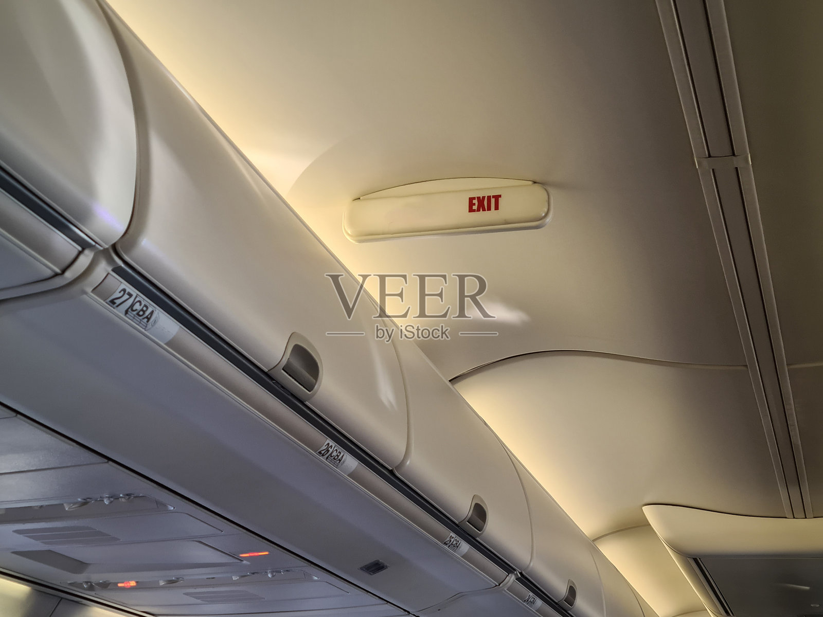 飞机客舱内部视图,突出显示飞行中的紧急出口标志和头顶储物空间照片摄影图片