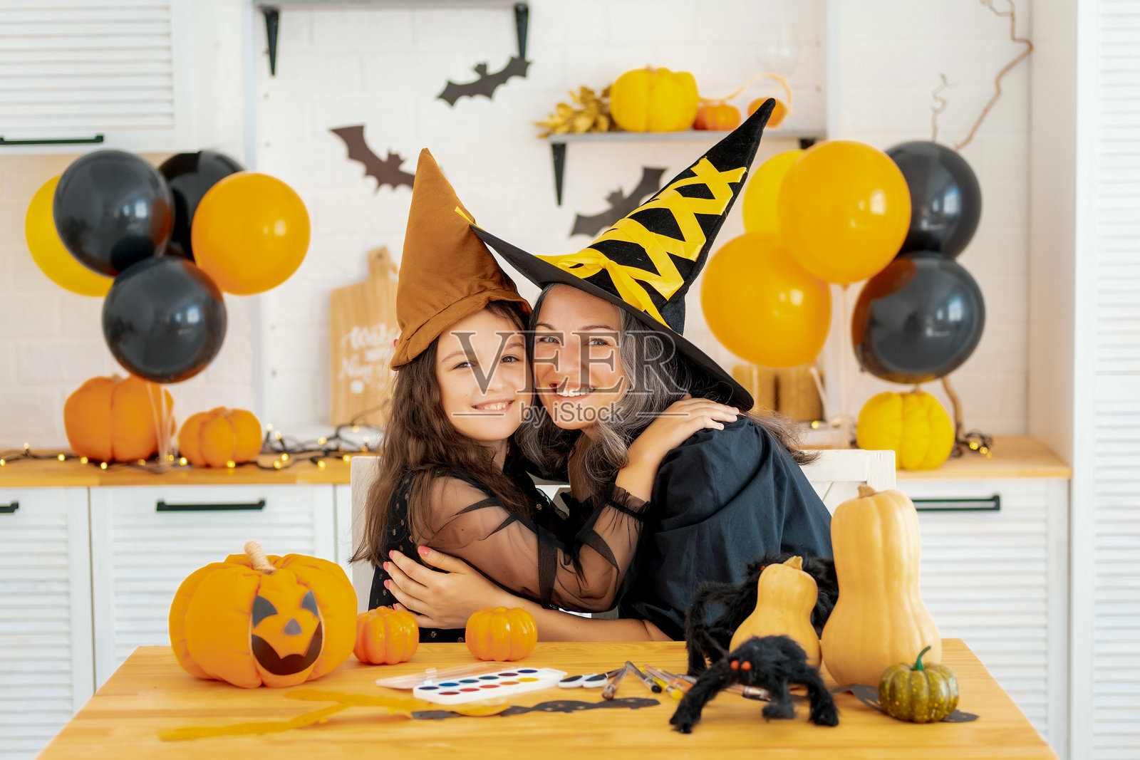 万圣节,一个穿着女巫服装的孩子和母亲正在为万圣节做准备,互相吓唬,拥抱并欢庆,祝贺彼此节日快乐,万圣节快乐。照片摄影图片
