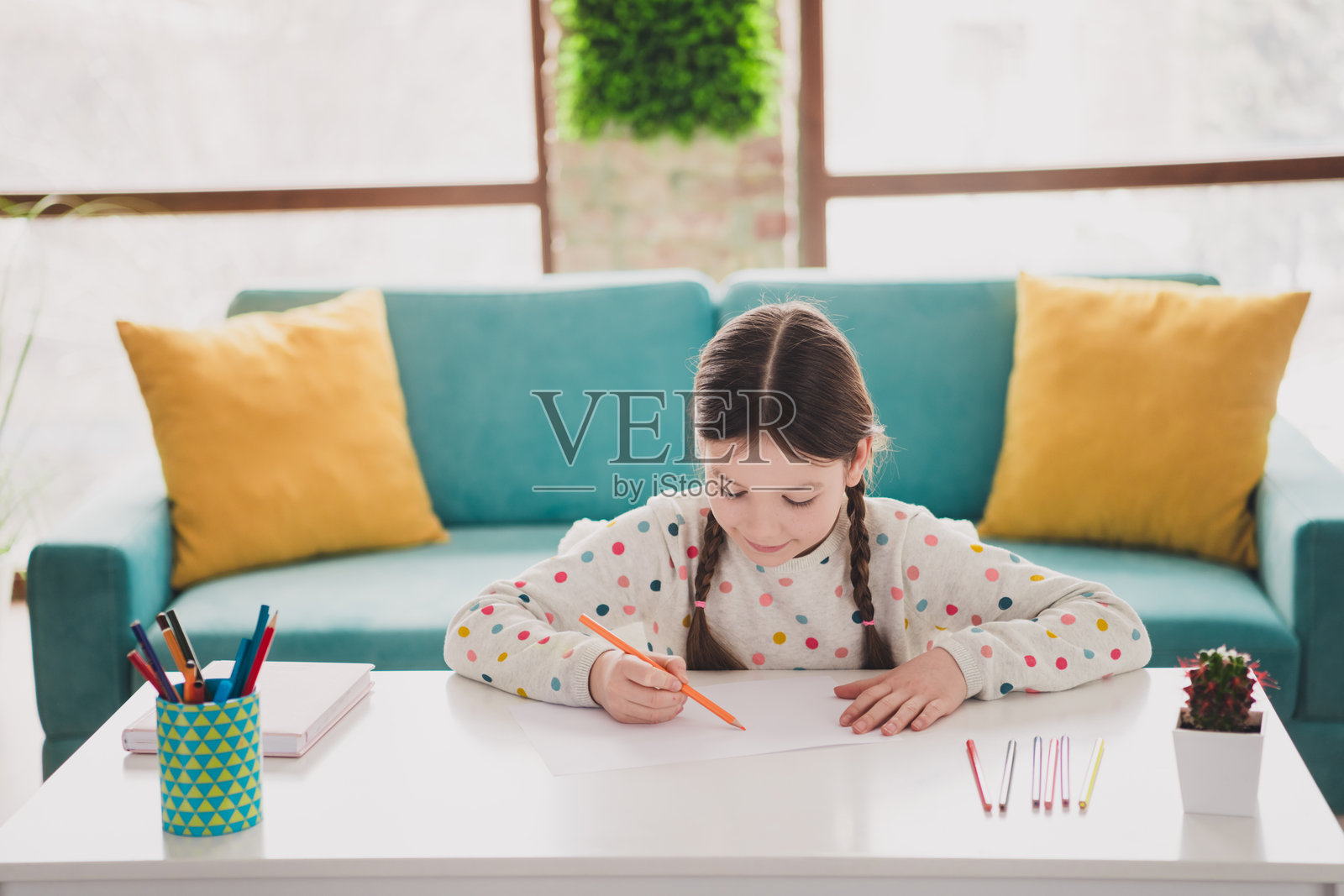 可爱的女孩在现代公寓室内穿着毛衣,手持铅笔进行绘画。照片摄影图片