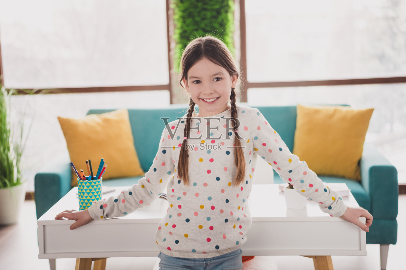 可爱的小女孩在现代公寓室内穿着毛衣,露出灿烂的笑容坐在桌子旁。照片摄影图片