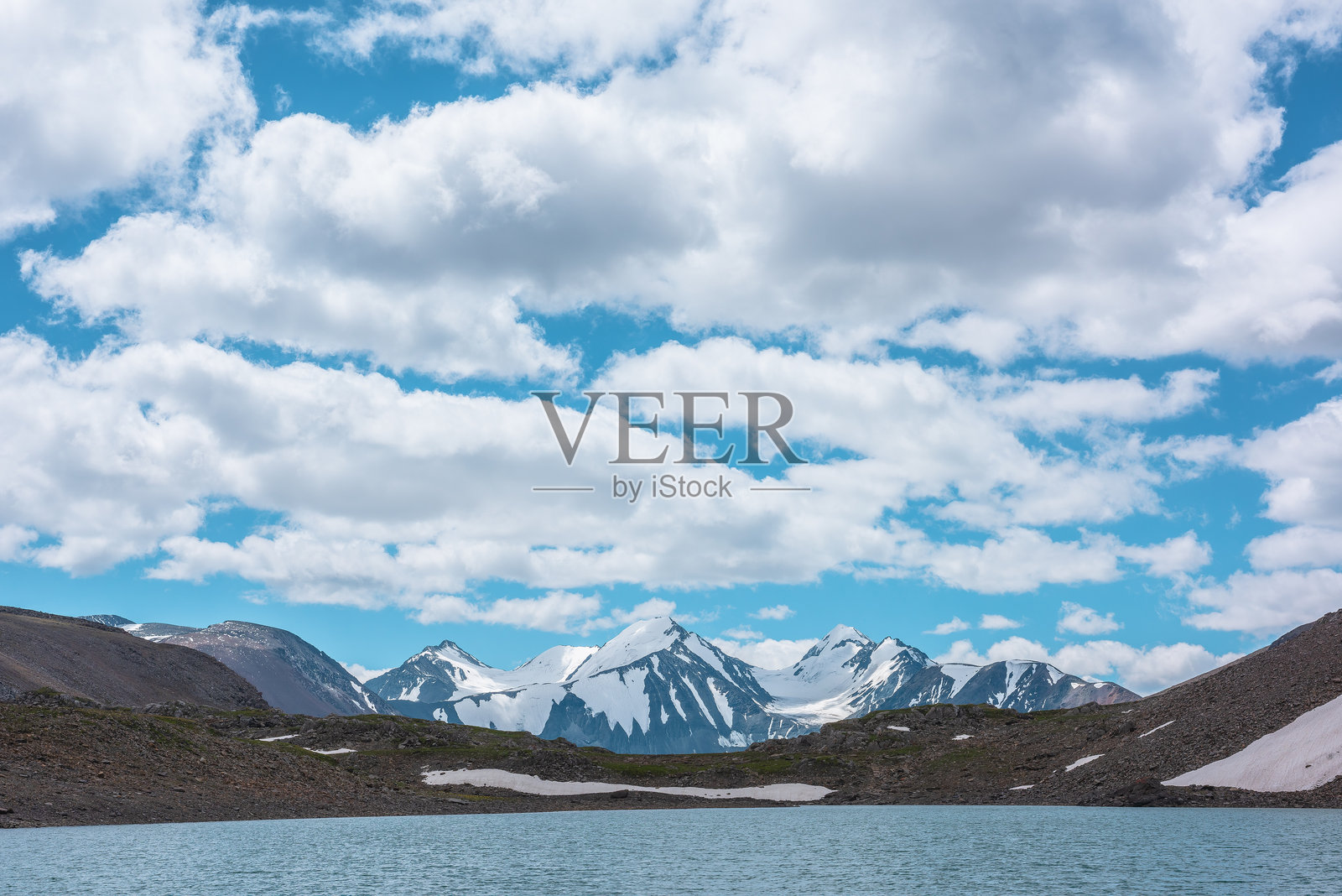 最美的景色:碧蓝的高山湖泊与雪覆盖的山脉和几座尖尖的山峰相映成趣。湖面上涟漪荡漾,湖水呈现出绿松石色,三座雪峰在多云的蓝天下显得格外壮观。照片摄影图片