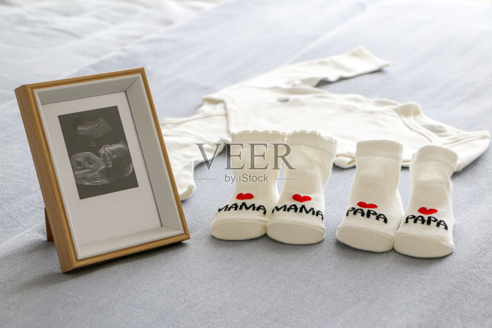 怀孕和分娩的准备与期待。框架中的超声波照片与新生儿衣物、印有“爱妈妈和爸爸”的婴儿袜子一起展示。母性、父性、为人父母、期待的概念。照片摄影图片
