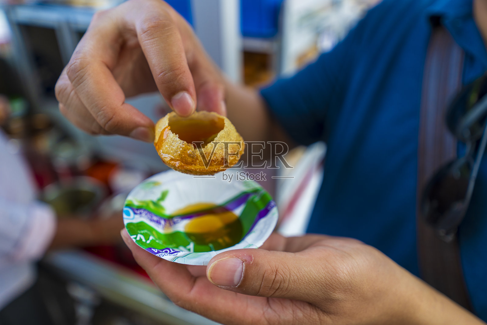 一个人正在将液体倒入一个空心的圆形脆饼中,脆饼被悬在一个铝箔碗上。这种传统的印度街头小吃在斋浦尔非常受欢迎。照片摄影图片