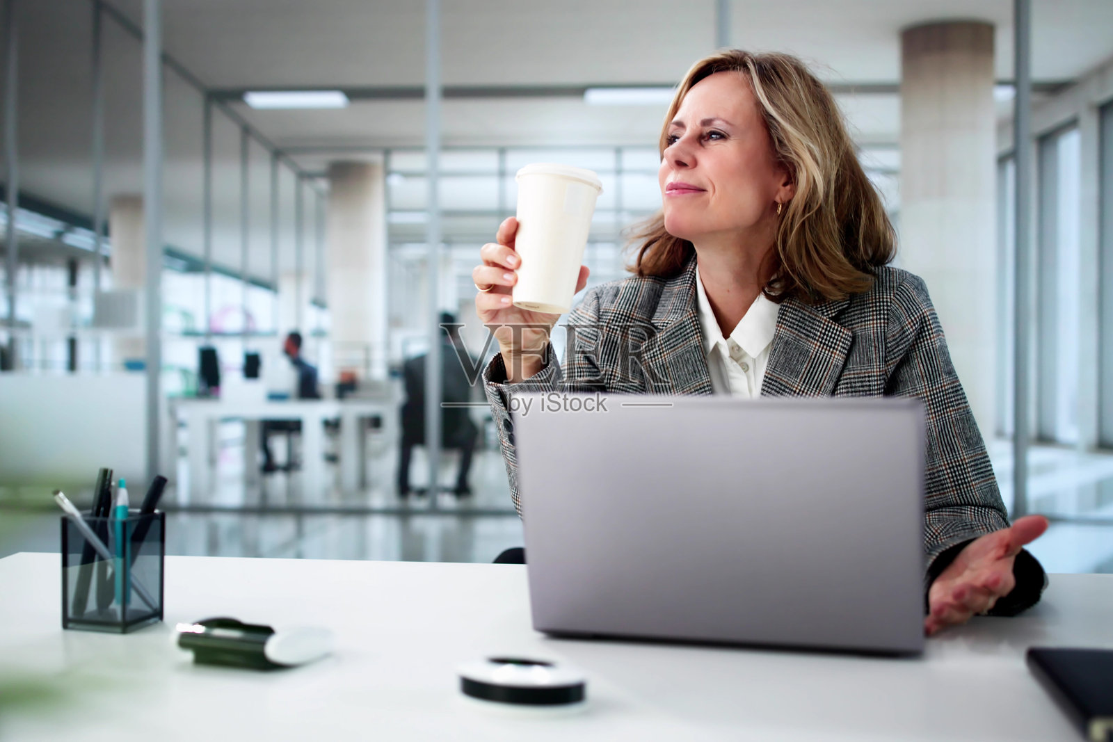 女商人在办公室桌子上使用笔记本电脑,喝咖啡。照片摄影图片