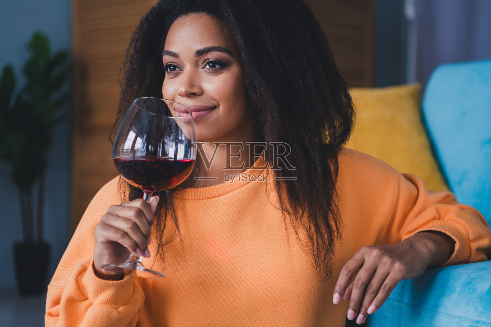 穿着橙色服装的迷人年轻女性坐在地板上,享受着红酒的香气,度过一个舒适的日光明媚的家居室内时光。照片摄影图片