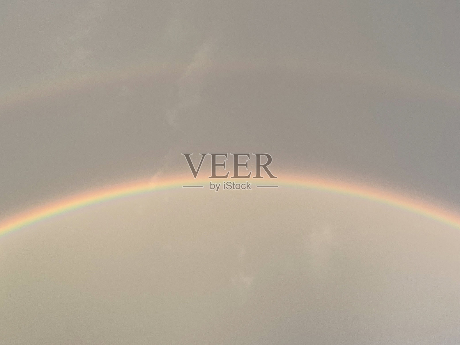 一幅令人惊叹的画面,淡淡的彩虹弯曲在柔和的多云天空中,唤起自然中的宁静与安详。照片摄影图片