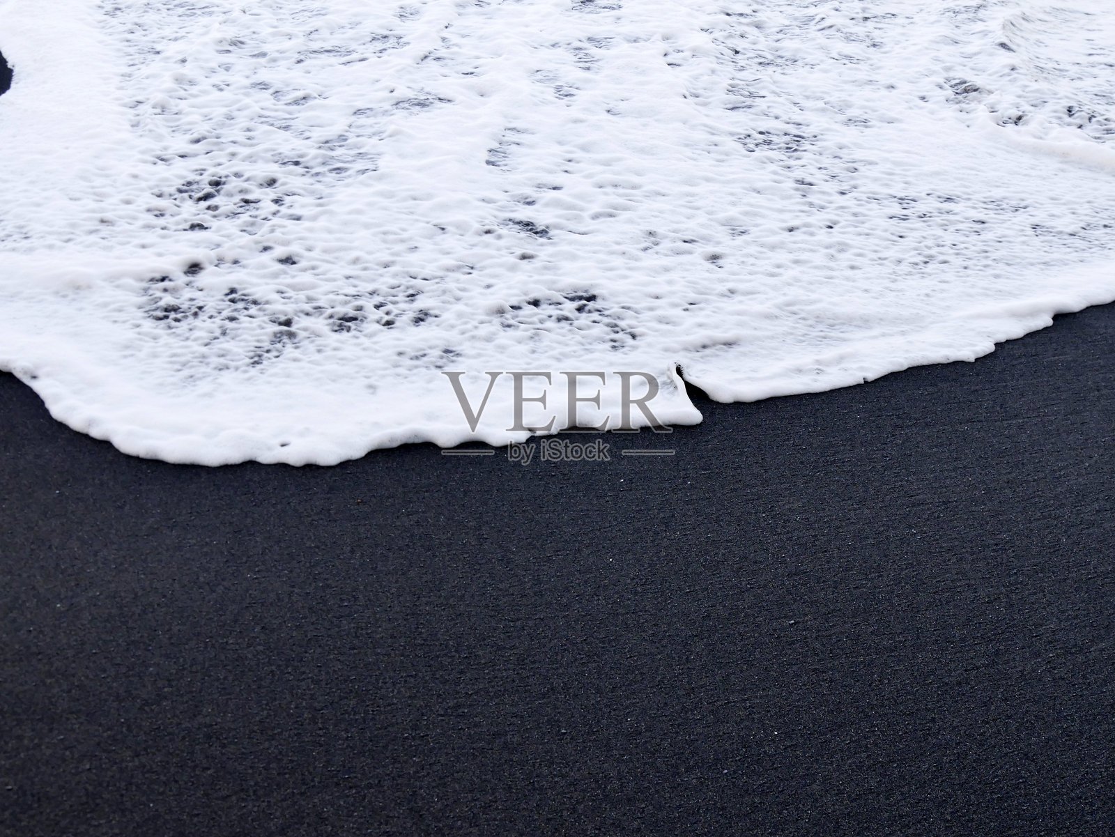 白色潮浪的泡沫在瓜德罗普的黑沙滩上撞击。火山沙由玄武岩组成,与海泡沫形成鲜明对比。照片摄影图片