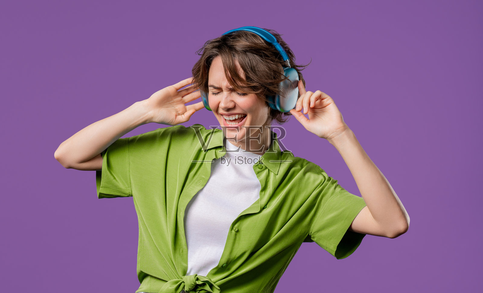 快乐的女人在紫色工作室背景下,戴着耳机享受音乐和舞蹈。无线现代音响技术,在线播放器。照片摄影图片