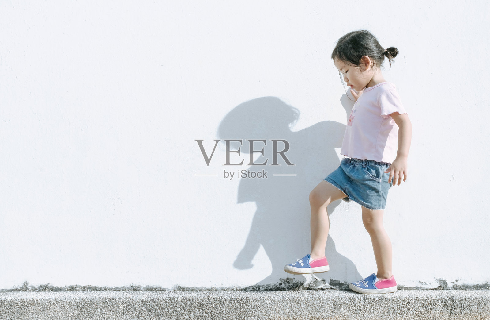 阳光明媚的日子里,女孩侧身走在挡土墙上照片摄影图片