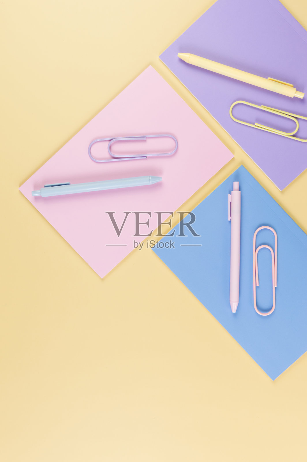 从上方俯视粉色、紫色和蓝色的笔记本,背景为黄色。粉色、黄色和蓝色的笔,回形针,学校和办公室的壁纸。照片摄影图片