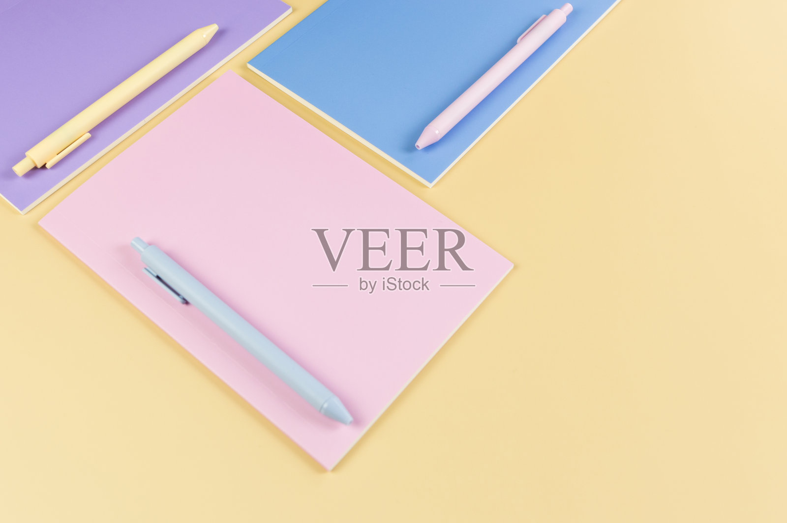 从上方俯视粉色、紫色和蓝色的笔记本,背景为黄色。粉色、黄色和蓝色的笔,学校和办公室壁纸。照片摄影图片