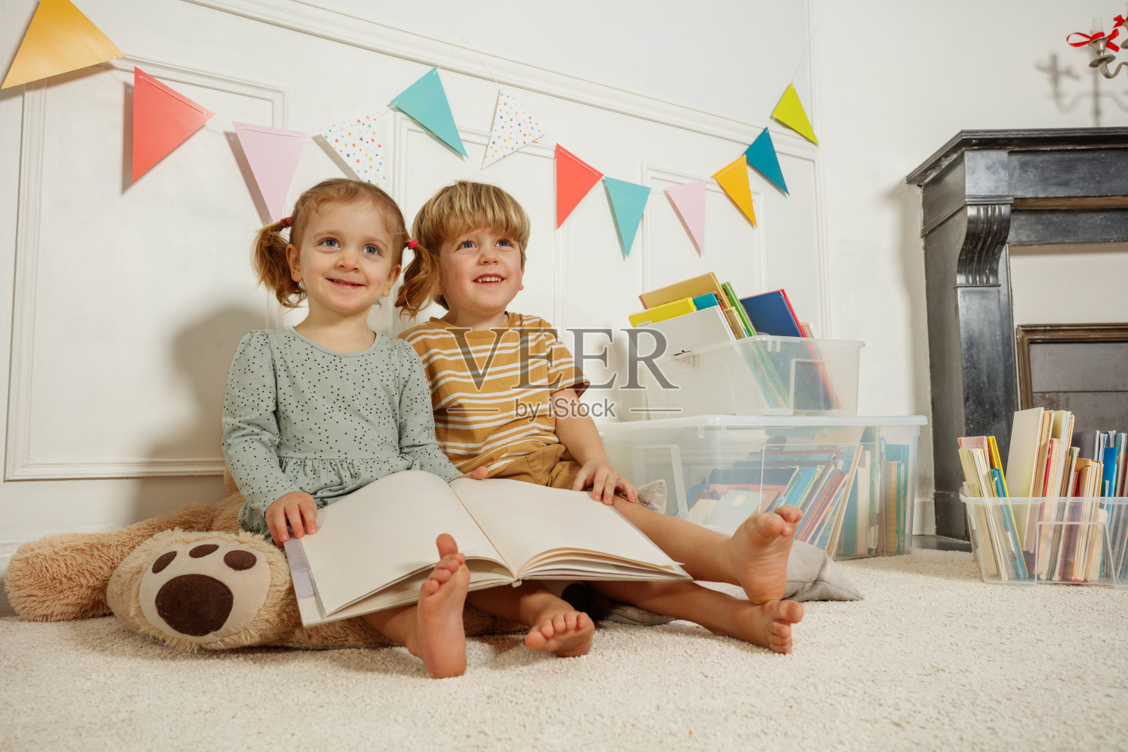 兄弟姐妹在明亮的卧室里微笑着享受故事时间,手中拿着书。照片摄影图片