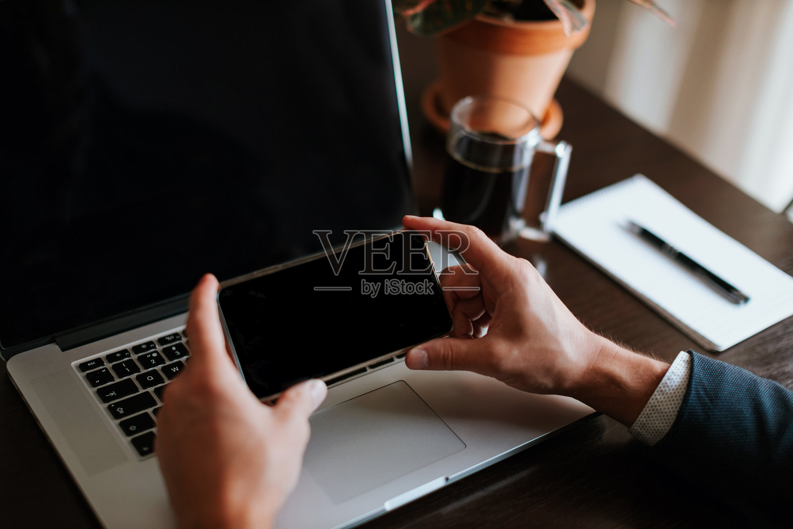 男子在办公室用手机的中部特写,旁边有笔记本电脑。照片摄影图片