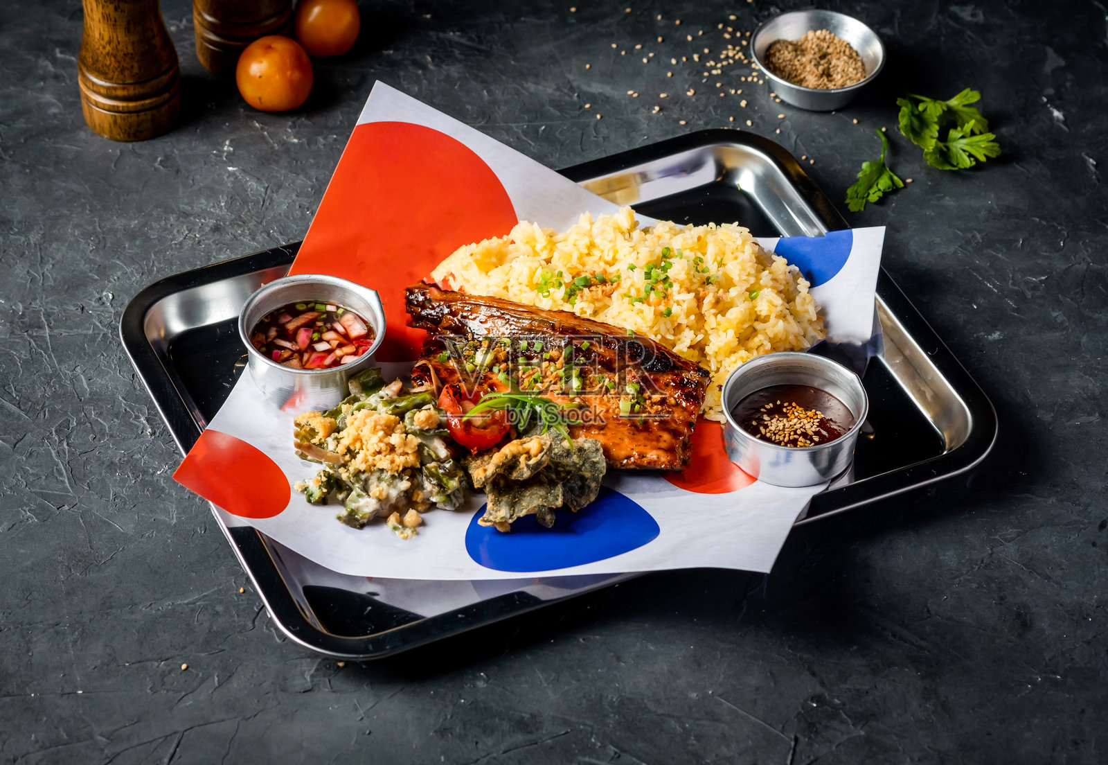 烤鲳鱼肚配蒜香米饭、配菜、香菜和酱汁,放在托盘上,背景为灰色,侧面视图的餐盘美食照片摄影图片