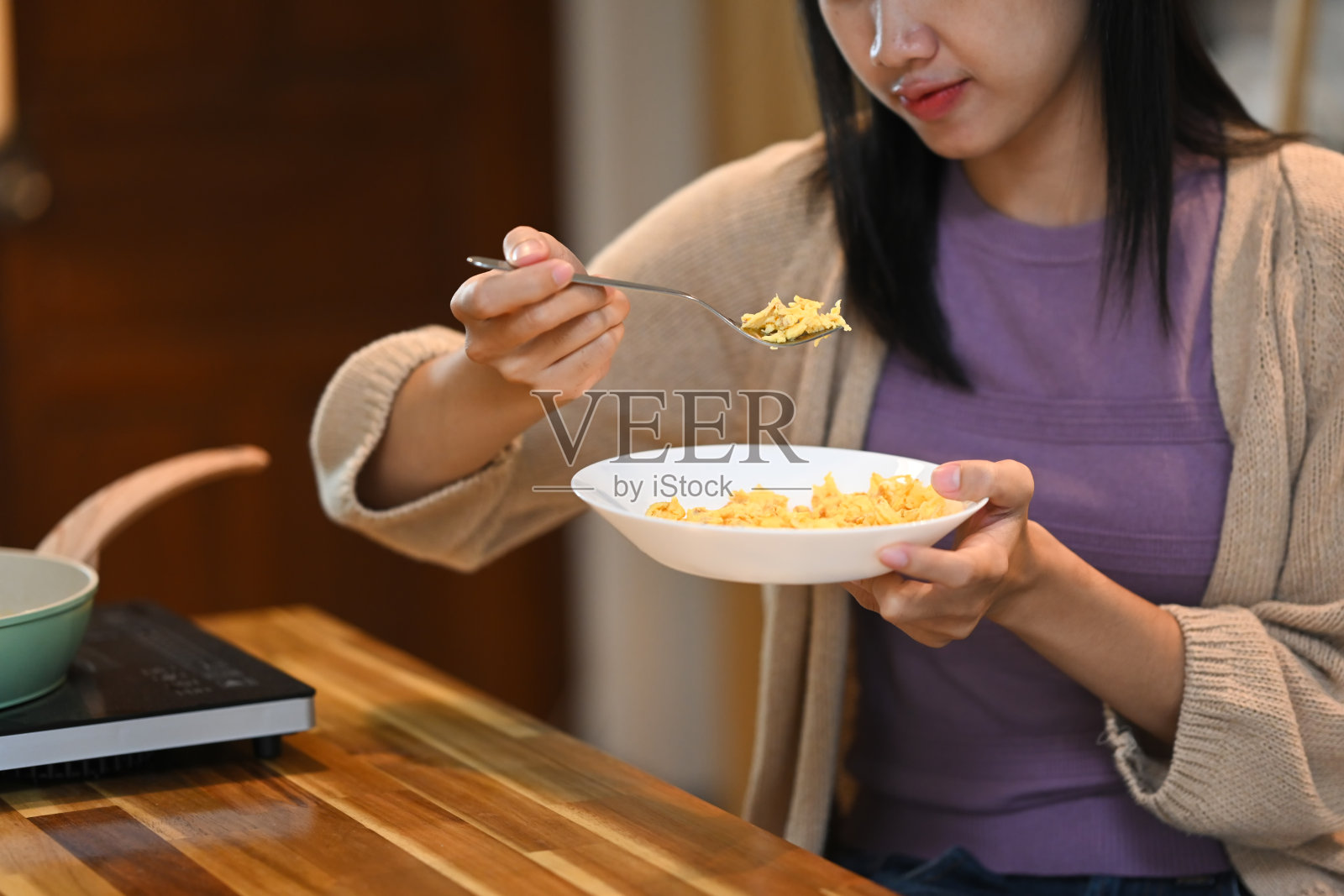 女人坐在木制厨房柜台旁,用叉子吃炒鸡蛋的局部照片照片摄影图片