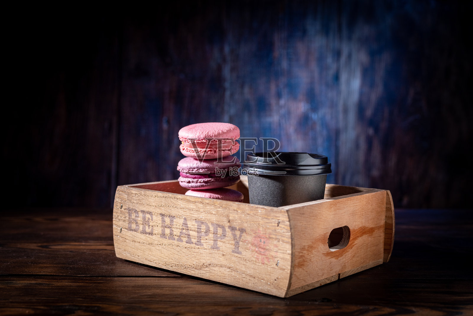 桌子上木托盘里的咖啡和马卡龙。黑色玻璃杯和粉色饼干。照片摄影图片