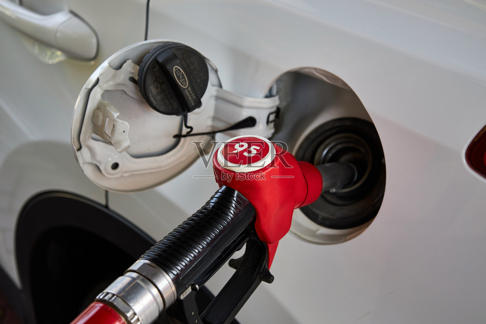 汽油加油机,红色燃油喷嘴插入白色汽车的油箱中,正在加注95号汽油。照片摄影图片