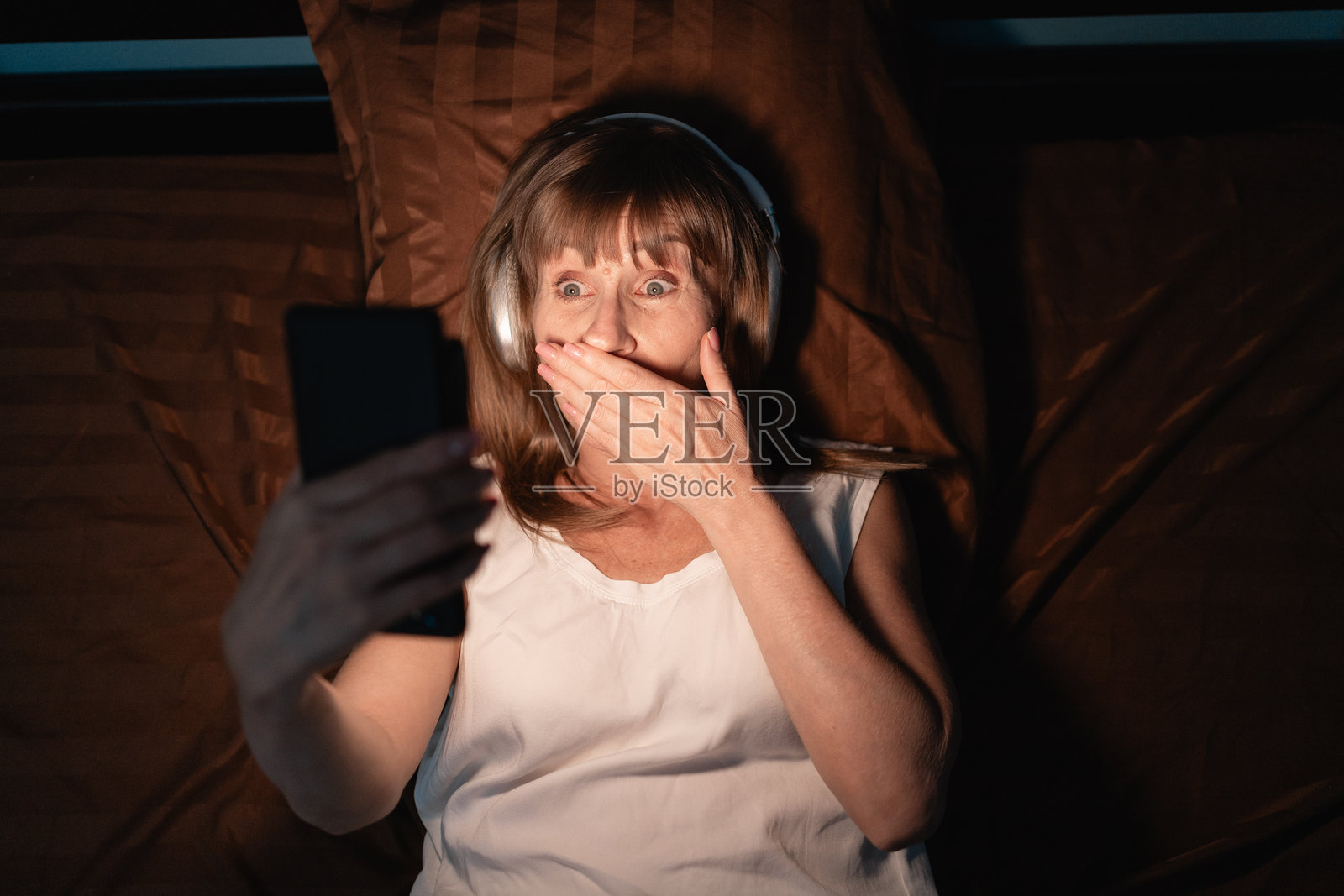 担心的女性在卧室的床上夜间用智能手机观看不良在线内容照片摄影图片