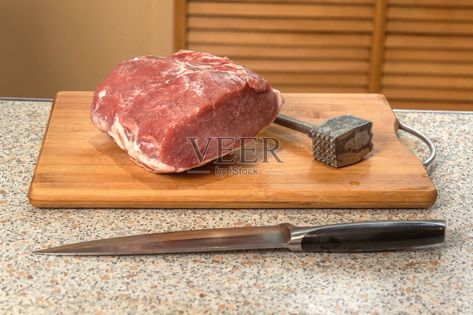 一块生猪里脊肉、一把刀和一个肉锤放在厨房砧板上。照片摄影图片