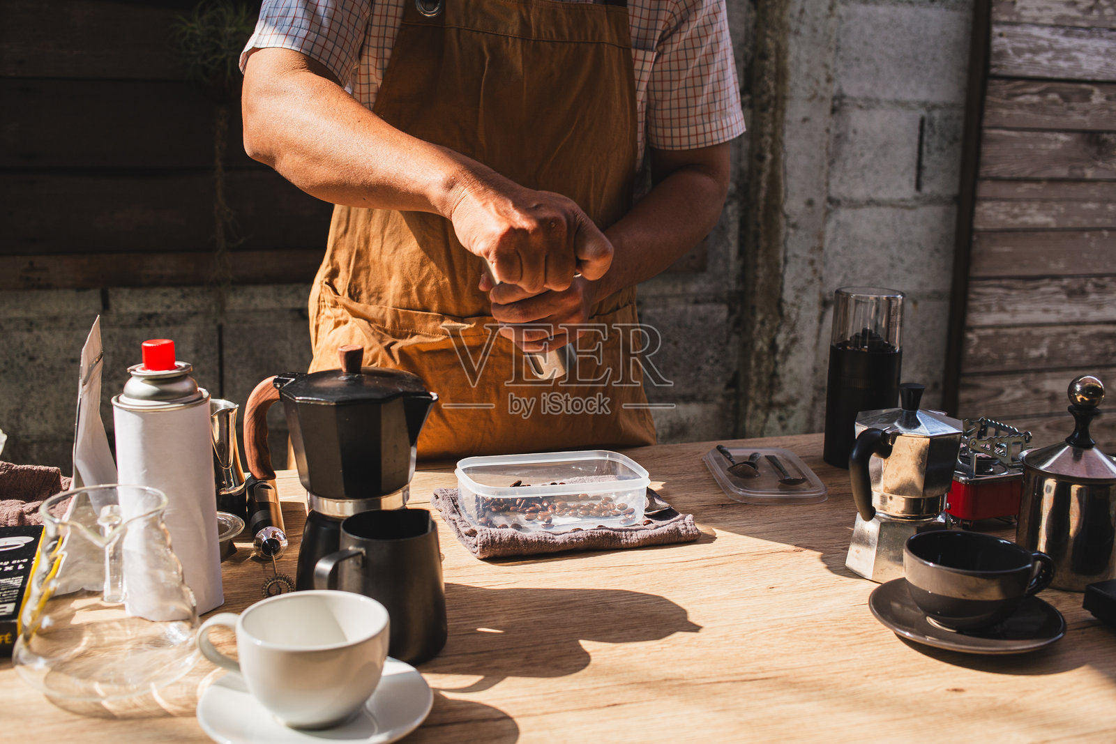 男子在一个乡村户外咖啡馆的环境中,用手动不锈钢磨豆机研磨烘焙好的阿拉比卡咖啡豆,准备一杯新鲜的咖啡,享受美味而芳香的咖啡体验。照片摄影图片