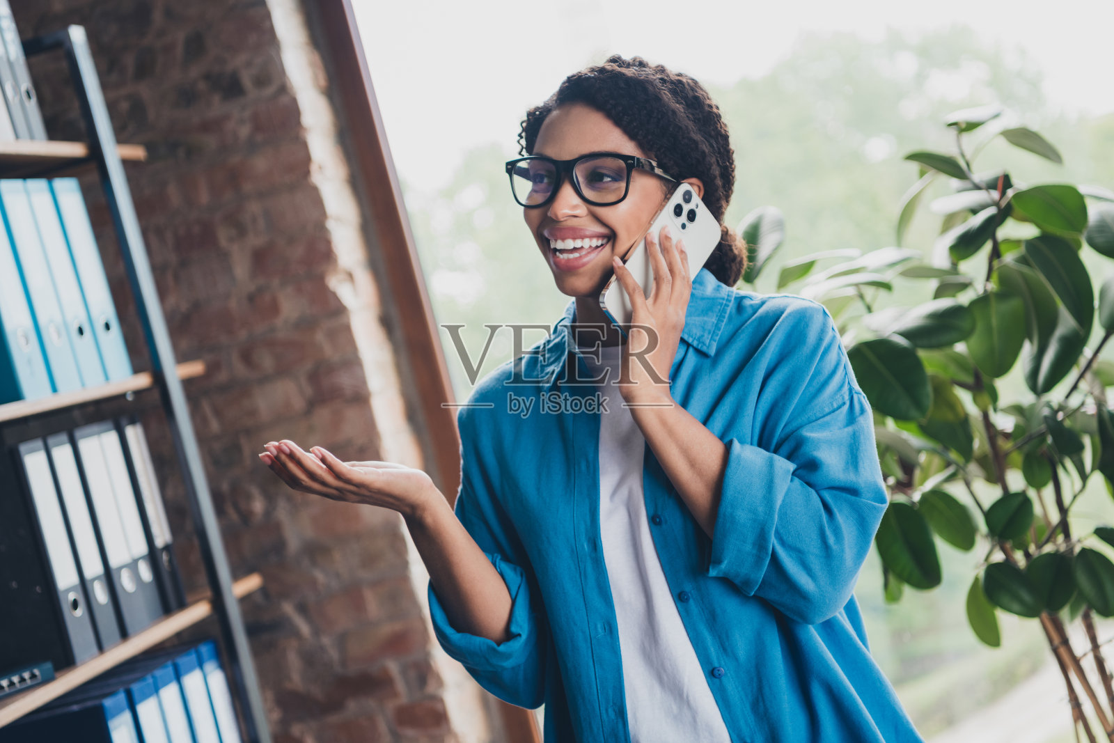 穿蓝色衬衫的年轻女子在明亮共享办公室打电话照片摄影图片