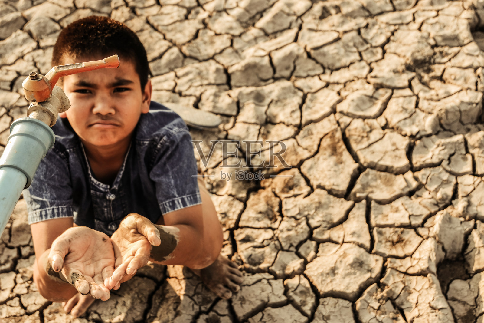 在干旱土地上,男孩双手托住水龙头下的水照片摄影图片
