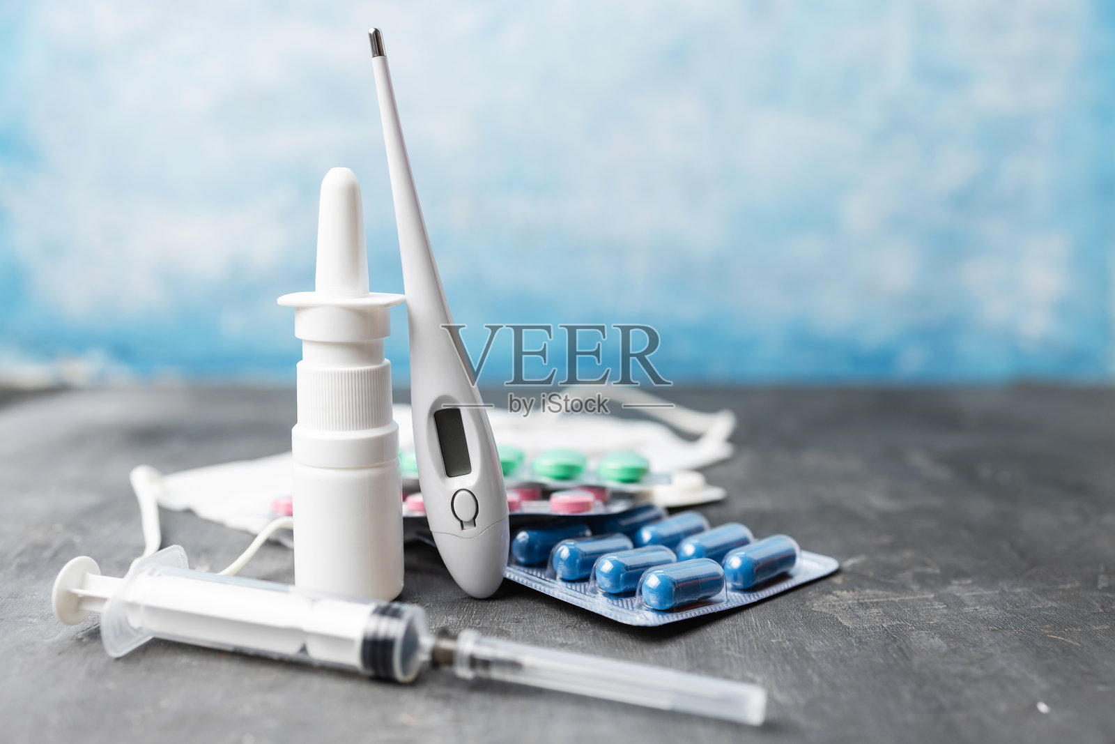 蓝色背景上的药房药品、鼻用喷雾剂、数字温度计、注射器、泡罩包装的药丸和医用口罩照片摄影图片