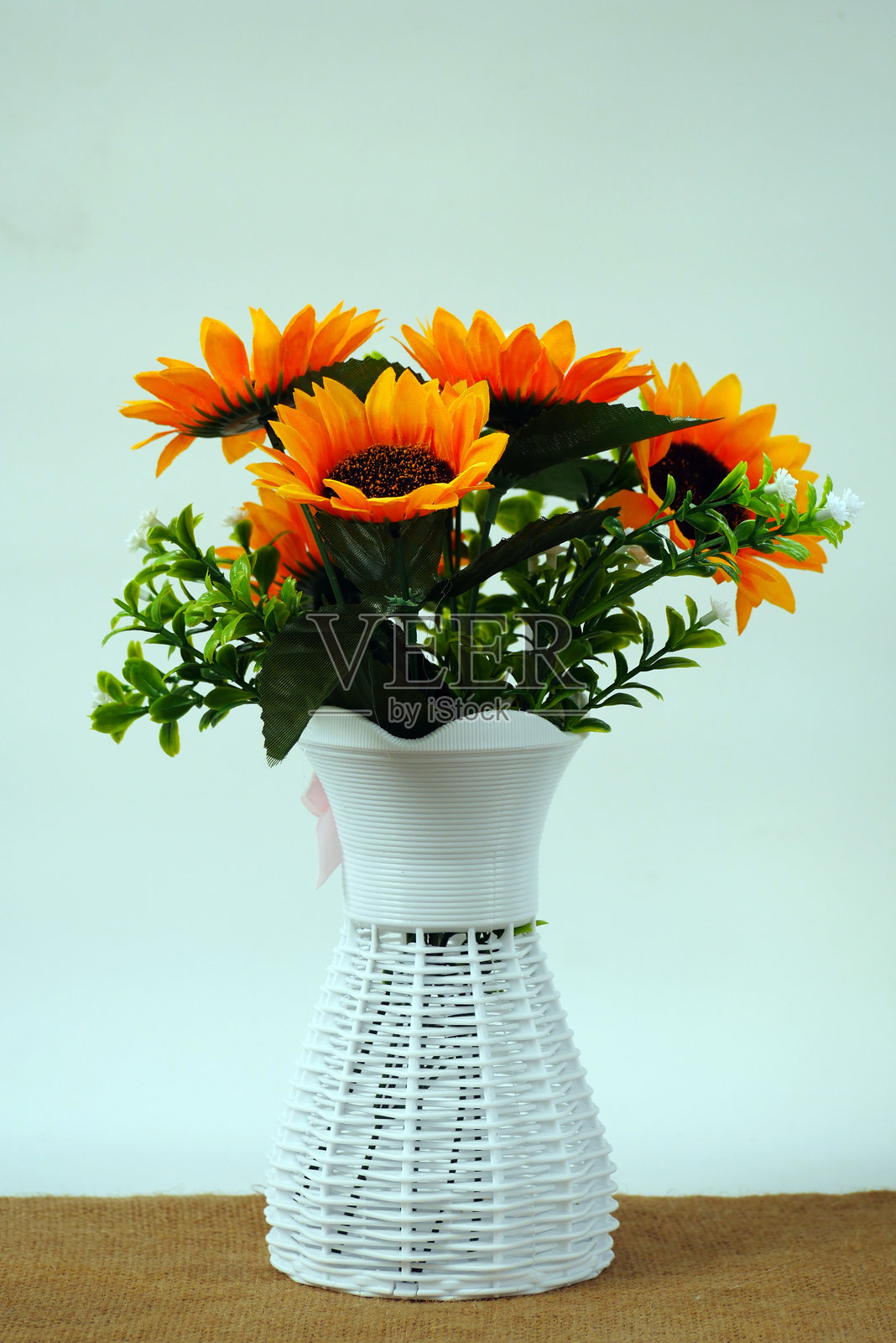 一束明亮而欢快的人造向日葵,插在一个白色编织花瓶中。照片摄影图片