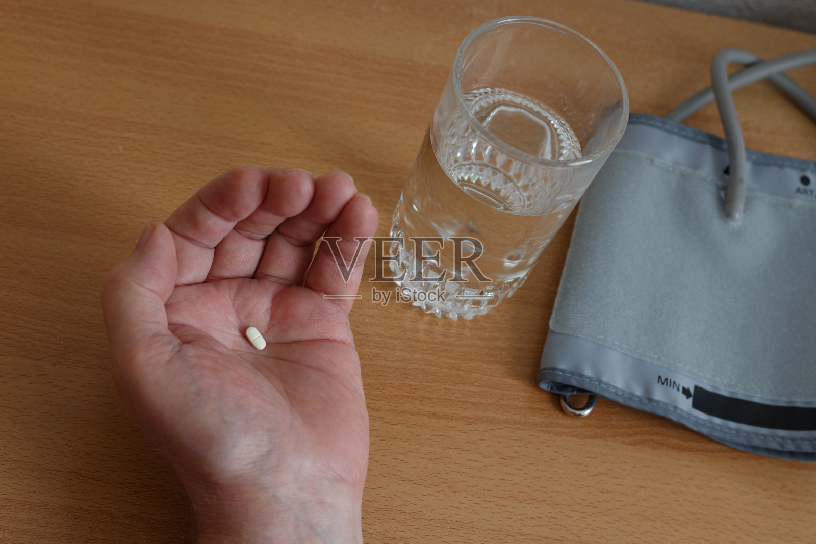 手中拿着药片,旁边是血压监测仪和一杯水。照片摄影图片