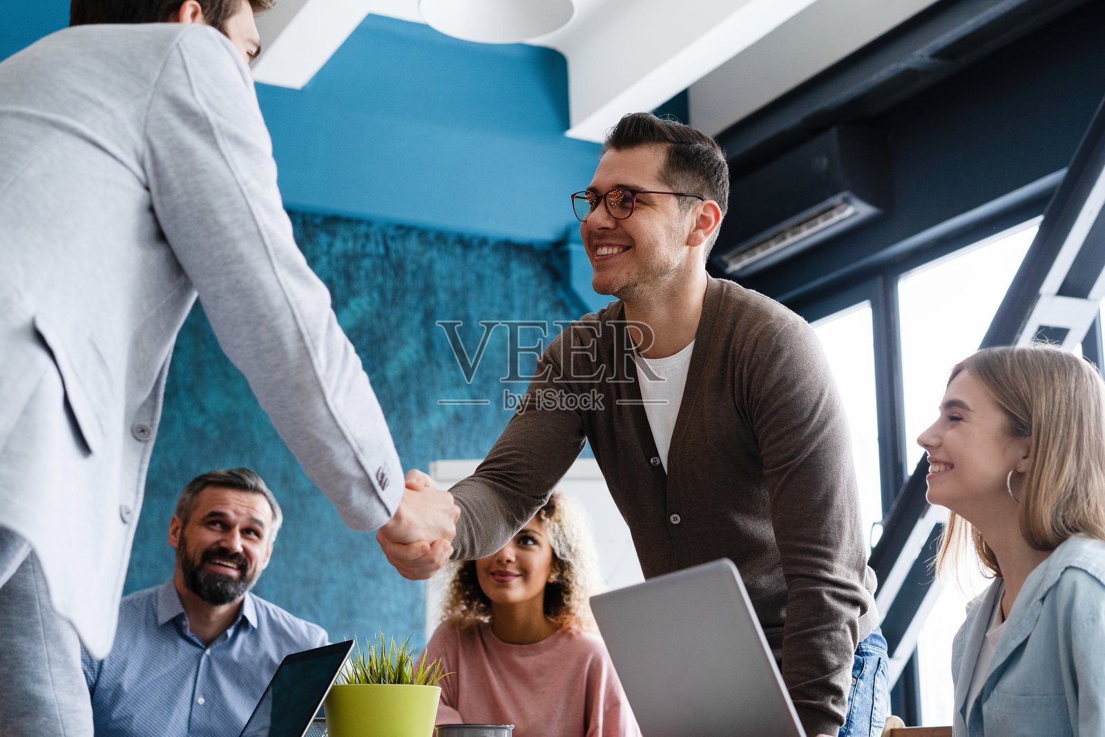 欢迎加入。自信的男性在办公室的桌子旁握手微笑。照片摄影图片