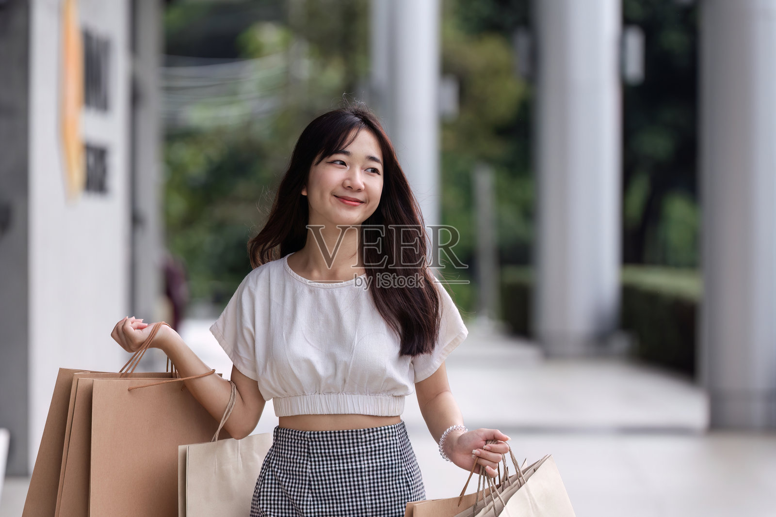 年轻女性在阳光明媚的日子里,手提纸袋在现代百货商店购物照片摄影图片