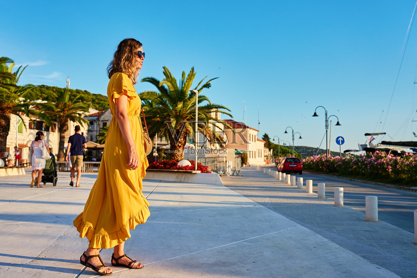 穿着黄色连衣裙的女人在阳光明媚的海滨小镇的长廊上漫步照片摄影图片