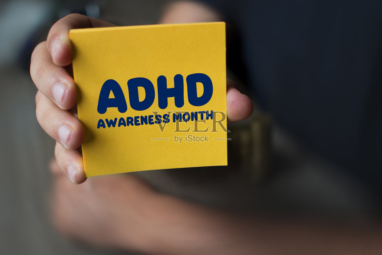 手持写有ADHD Awareness Month(多动症宣传月)的黄色纸张照片摄影图片