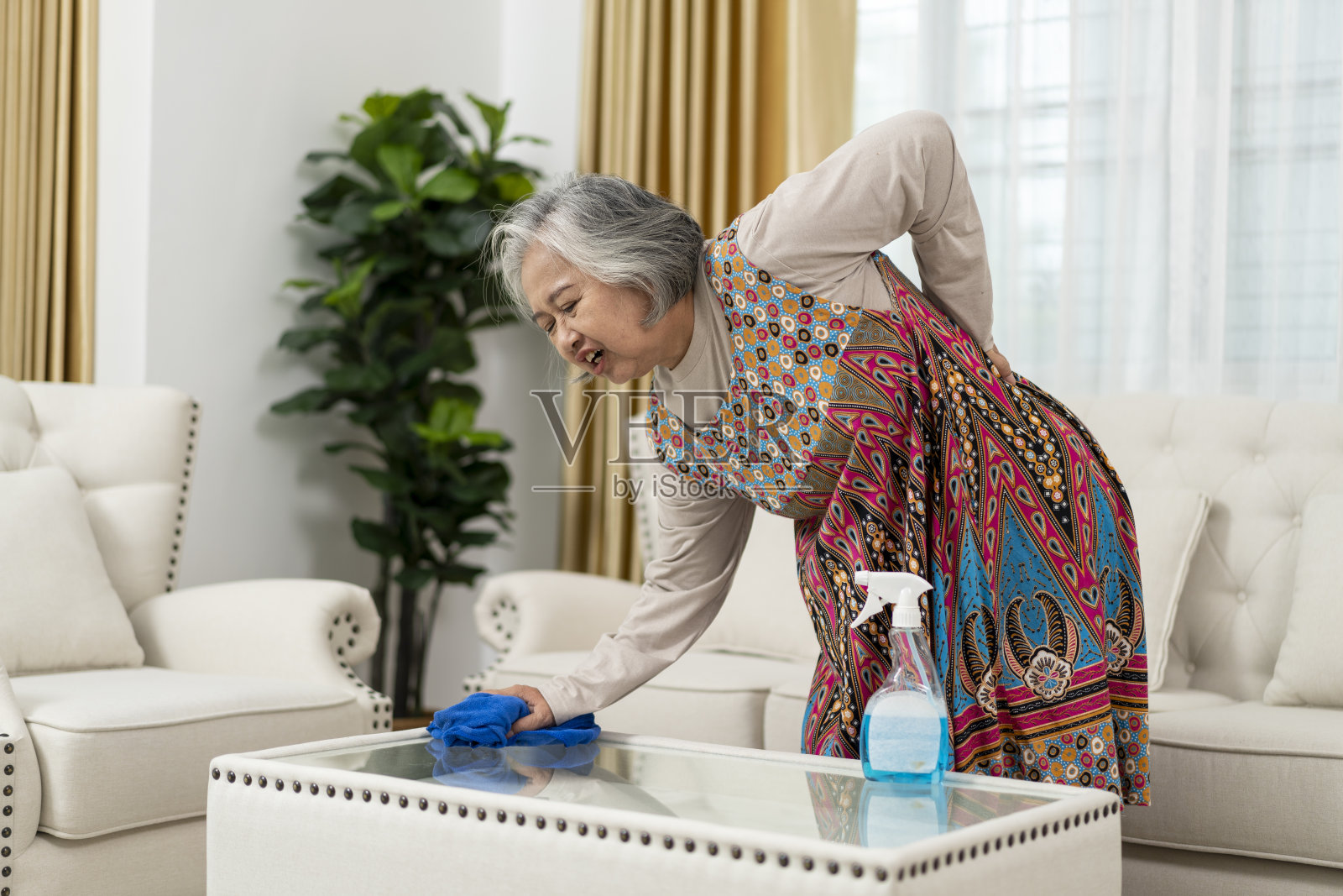 老年女性在客厅清洁玻璃桌子时感到背部疼痛照片摄影图片