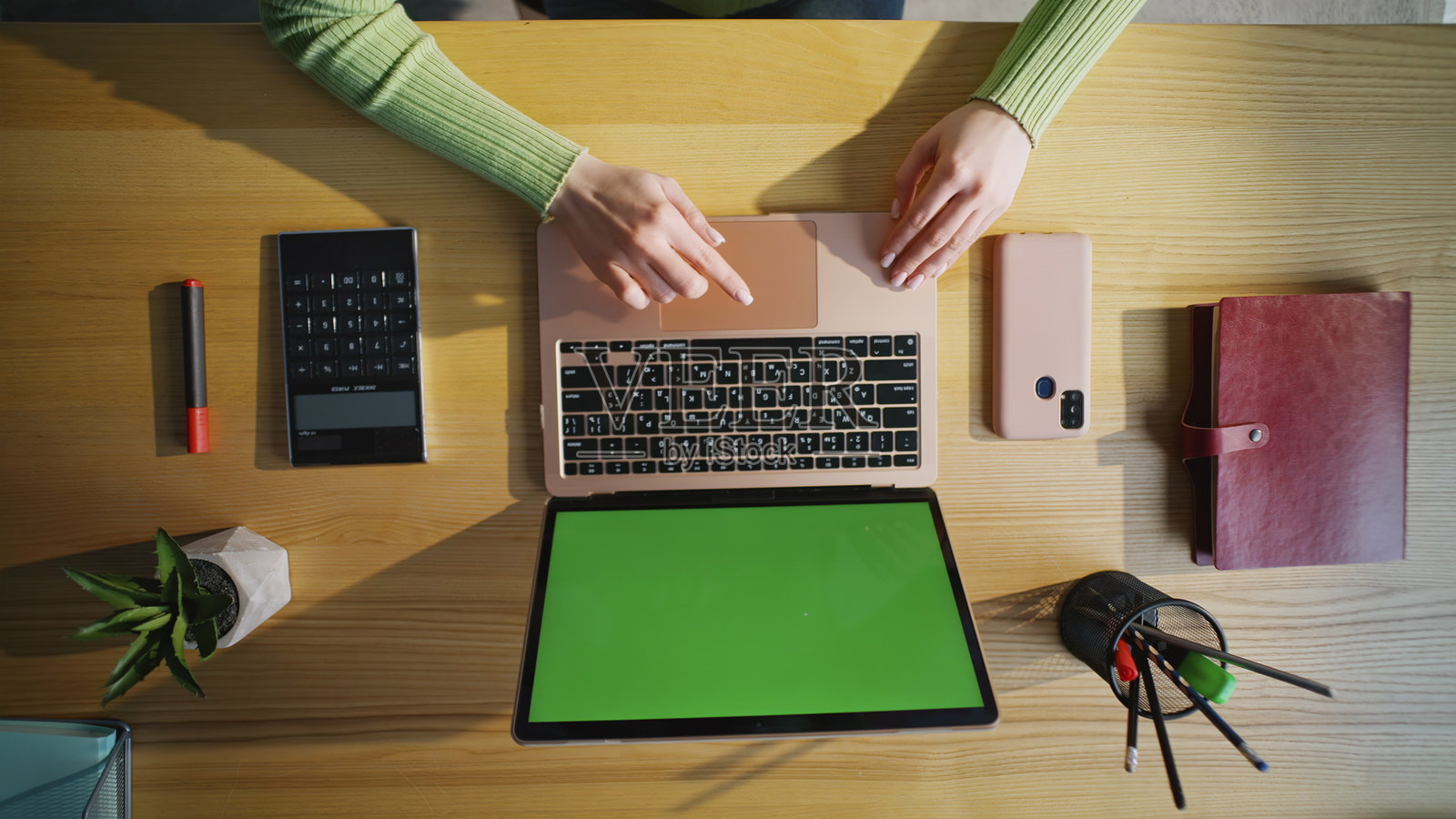 女士的手在木质办公桌上触碰绿幕笔记本电脑,俯视特写。照片摄影图片