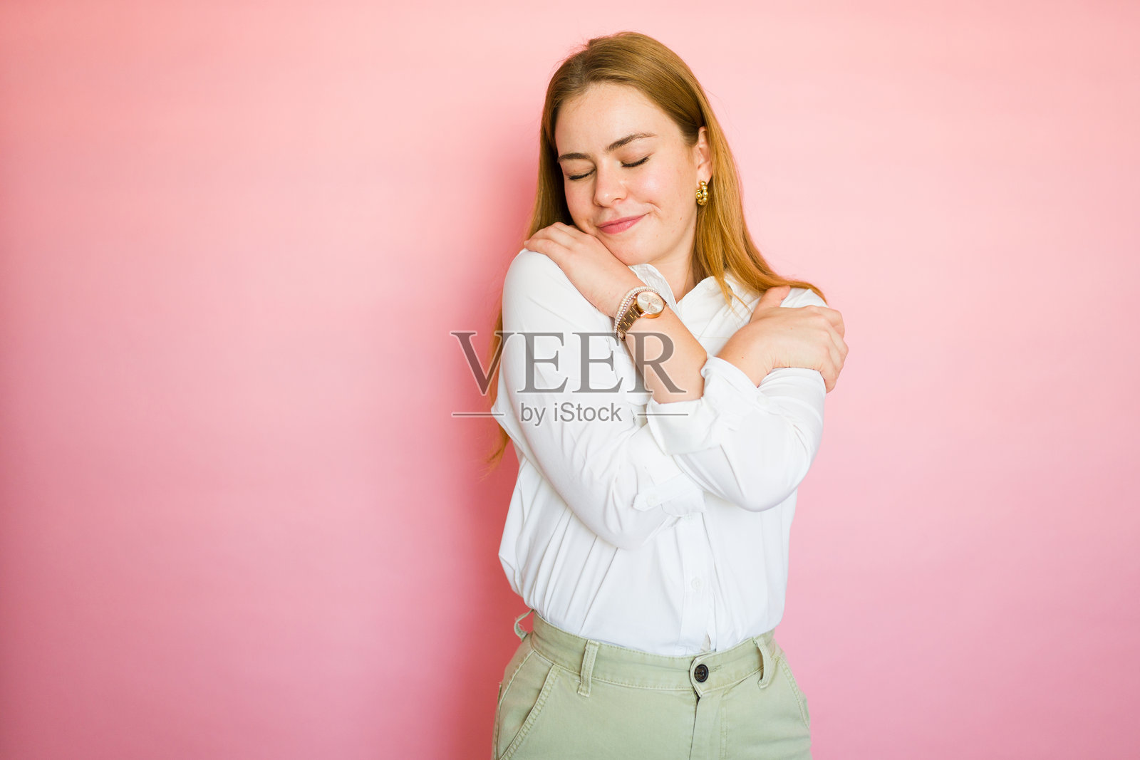 宁静的年轻女性微笑着拥抱自己,展现出自爱和自我接纳的状态。照片摄影图片