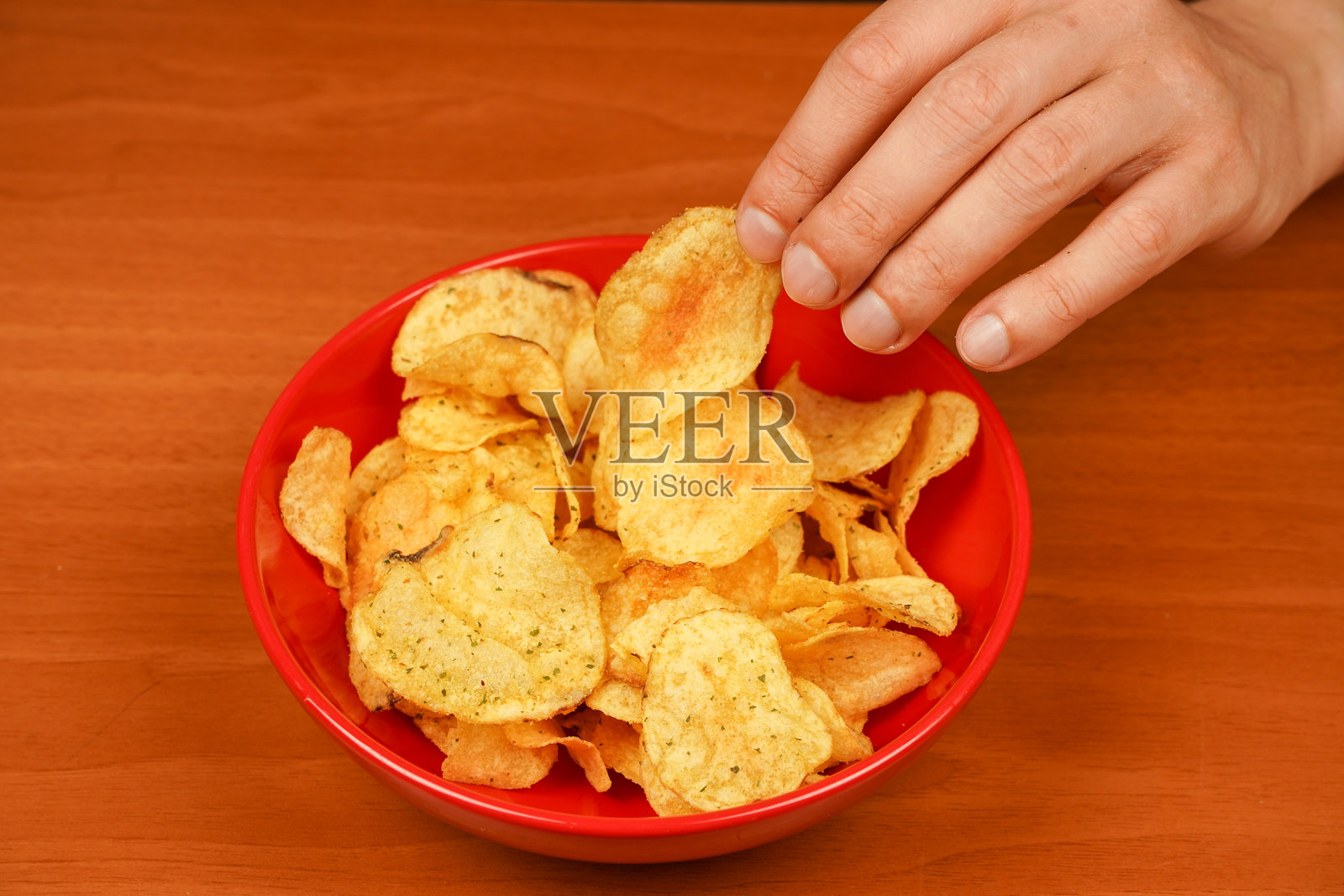 男人在吃薯片。手里拿着薯片。手从碗里拿出薯片的视角。快餐。垃圾食品。不健康的生活方式。卡路里。肥胖。美国食品。照片摄影图片