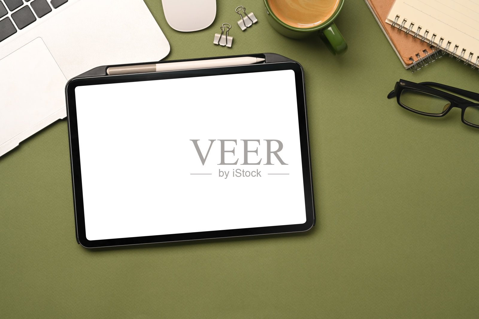 时尚的工作空间,绿色背景上有数码平板、咖啡杯、记事本和笔记本电脑。照片摄影图片