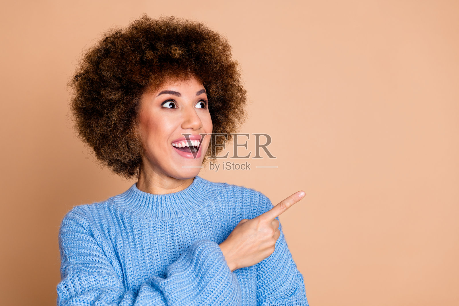 穿着蓝色针织毛衣的女孩,头发蓬松,惊讶地看着空旷的销售空间,背景为柔和的色彩。照片摄影图片