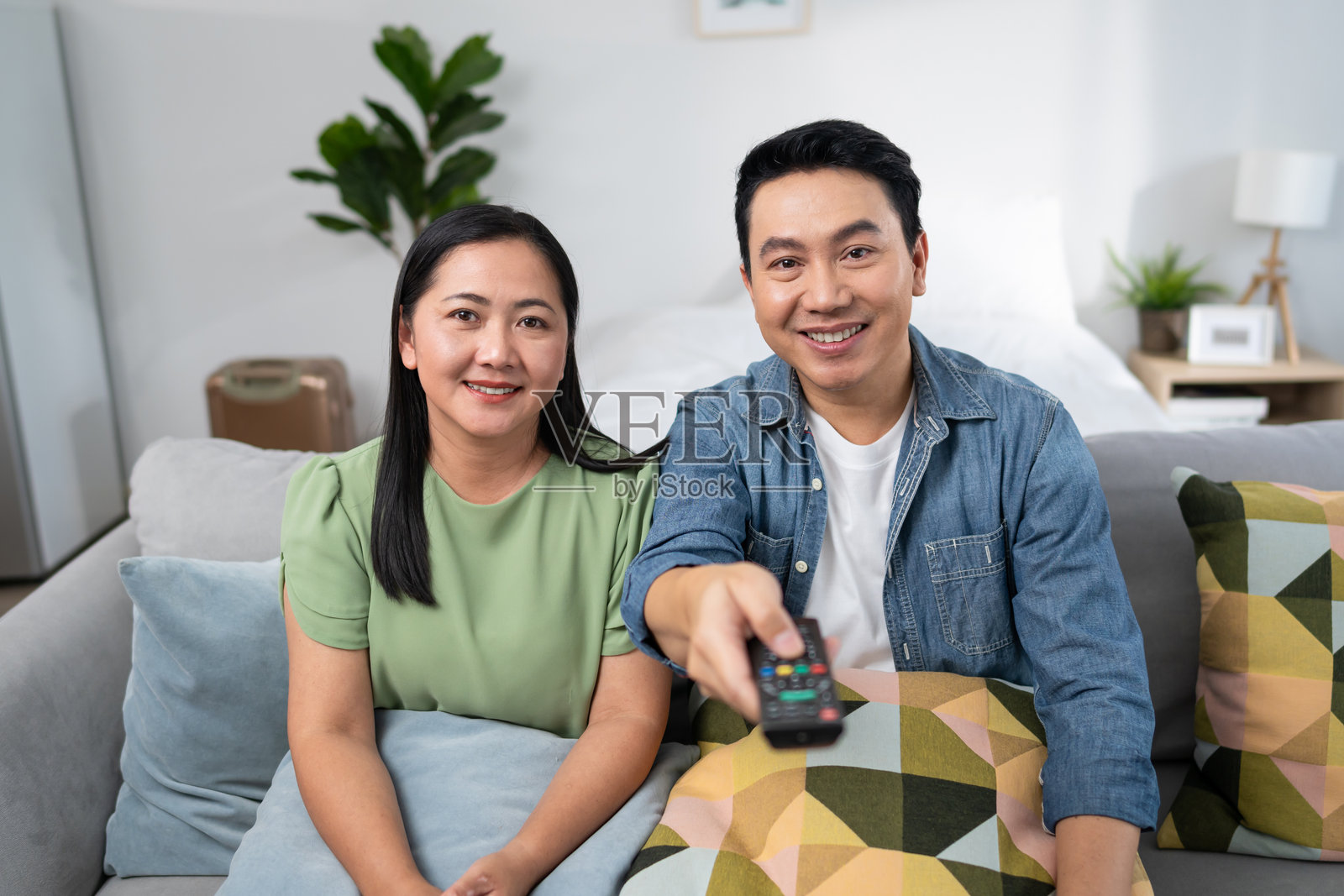 亚洲成熟的恩爱情侣在家中的客厅一起看电影。迷人的浪漫男女坐在沙发上,观看电视节目,周末在家里一起欢笑,享受乐趣。照片摄影图片