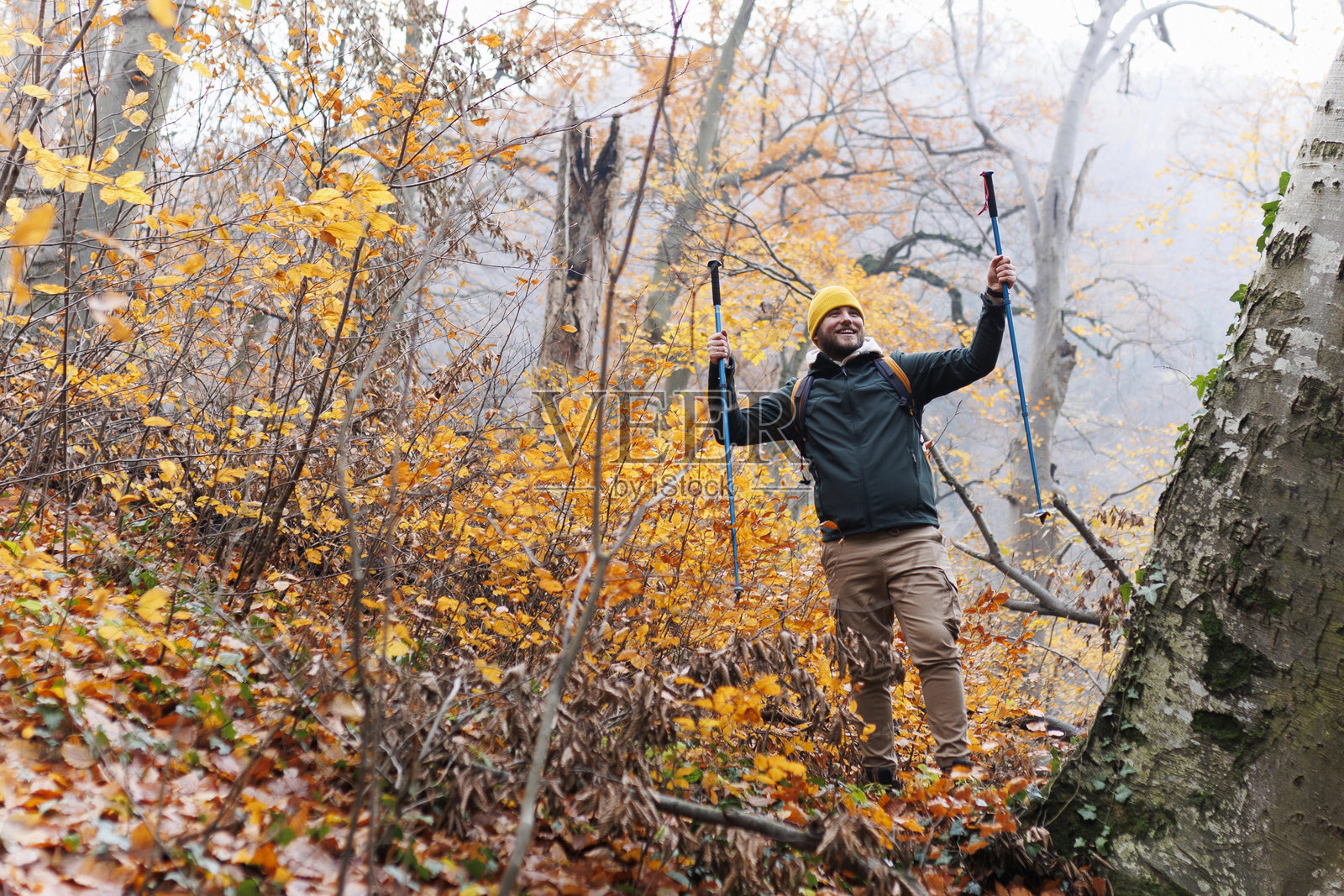 自信的年轻男子在山上行走,他使用登山杖并背着背包,体现自由与运动的概念照片摄影图片