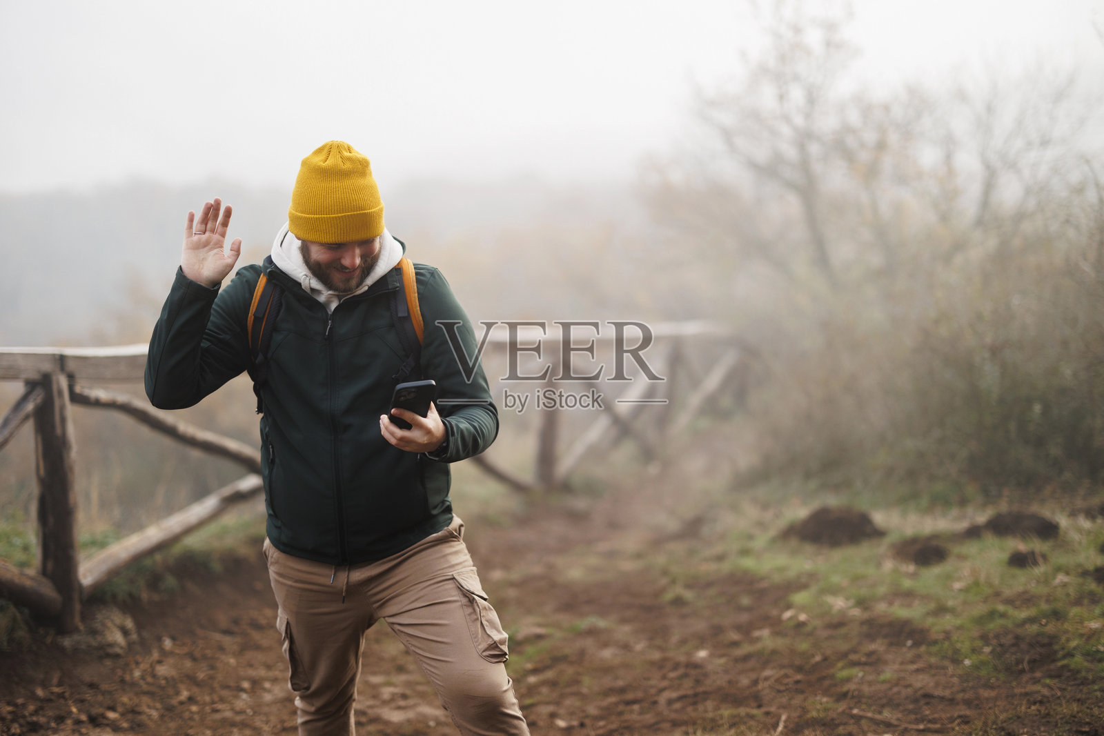 男人在山上徒步行走,他使用登山杖并背着背包,享受自由和运动,同时使用智能手机。照片摄影图片